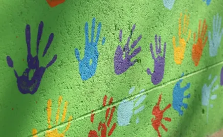 green brick wall with colourful hand prints painted on