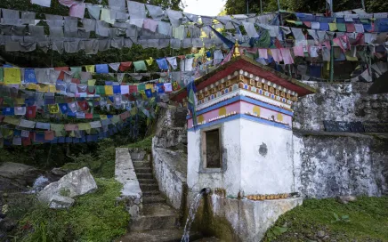 Rows of Buddhist prayer flags are hung in the sky behind a small white temple on a hill