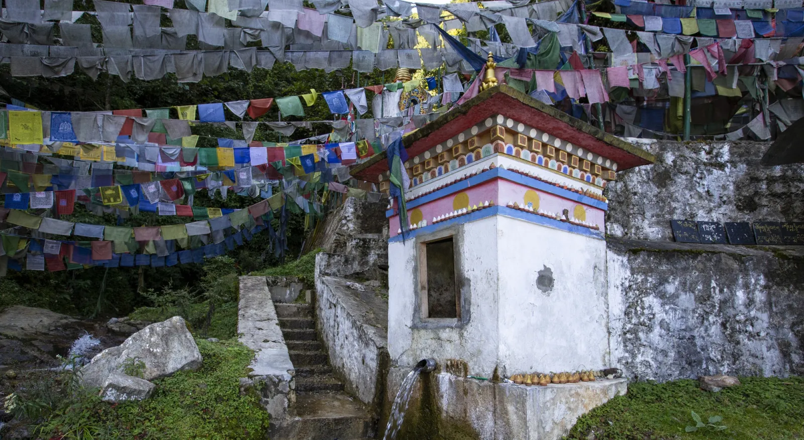 Rows of Buddhist prayer flags are hung in the sky behind a small white temple on a hill