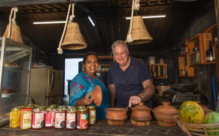 A man and a woman stand behind a table which has food and drinks on it. Both are smiling.