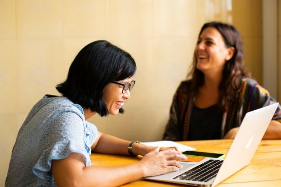 Two people smiling while sitting at desk with computer.