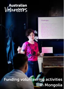 The cover page of the linked document. It includes the Australian Volunteers logo, and the title of the document: 'Funding volunteering activities in Mongolia'. The background image is of a woman standing next to a digital screen and gesturing as she presents to colleagues in a room.