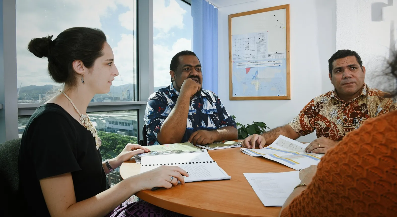 A lady and two men sit around a board table in discussion.