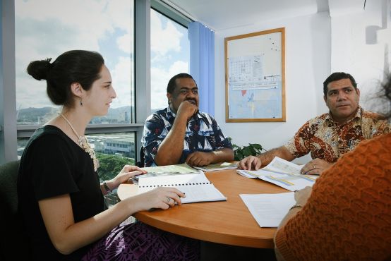 A lady and two men sit around a board table in discussion.