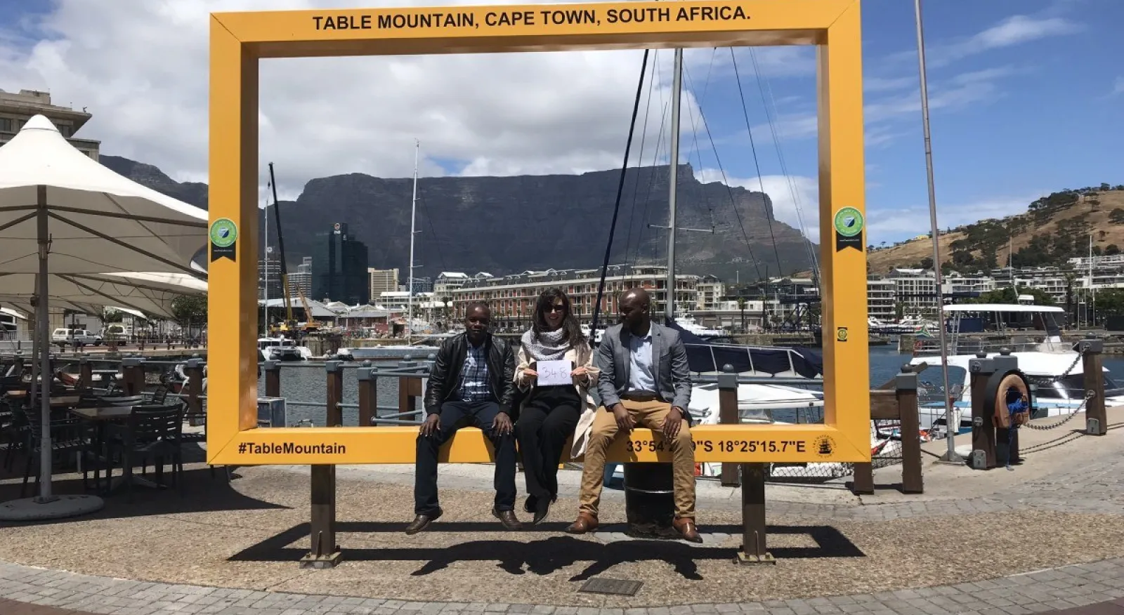 Three people pose for a photo in front of a large frame in Cape Town, South Africa.